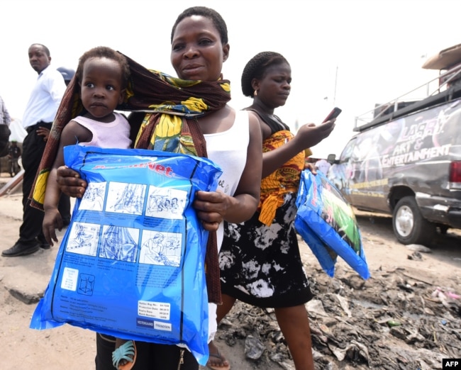 FILE - A woman carrying a baby holds a treated mosquito net during a malaria prevention event at Ajah in Eti Osa East district of Lagos, Nigeria, April 21, 2016.