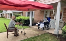 Trong mùa đại dịch, tháng bảy ở Mỹ không có mưa ngâu, nàng trên xe lăn, chàng vịn walker, Ngưu Lang Chức Nữ thời hiện đại, cả hai chỉ có 15 phút nhìn nhau bên ngoài cửa nursing home Ashbrook, New Jersey. [photo by Trần Qúi Thoại 2021]