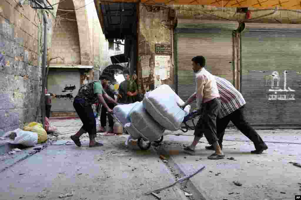 这张摄于2012年9月24日的照片显示，在叙利亚阿勒颇古城露天市场，一名自由叙利亚军战士(左)帮助商贩(右)把货物从他们的店铺里搬走。