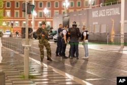 Police officers and a soldier stand by the sealed off area of an attack after a truck drove on to the sidewalk and plowed through a crowd of revelers who'd gathered to watch the fireworks in the French resort city of Nice, southern France, Friday, July 15, 2016.