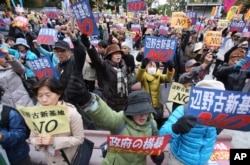 FILE - Anti-U.S. base protesters hold placards with a slogan that reads: "No to Henoko new base" during a rally in Tokyo.