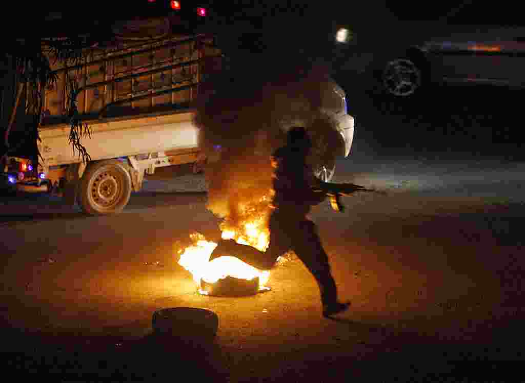 Seorang pemberontak Suriah berlari membawa senajta AK-47-nya ke arah pos pemeriksaan di pinggiran kota Damaskus (17/2) (AP).
