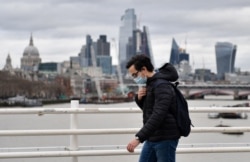 FILE - A pedestrian uses Waterloo Bridge to cross over the River Thames, backdropped by skyscrapers and offices of London on Jan. 29, 2022.