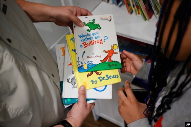 Tim McNeeley, left, helps students pick books to read during an after-school literacy program in Atlanta on Thursday, April 6, 2023. (AP Photo/Alex Slitz)