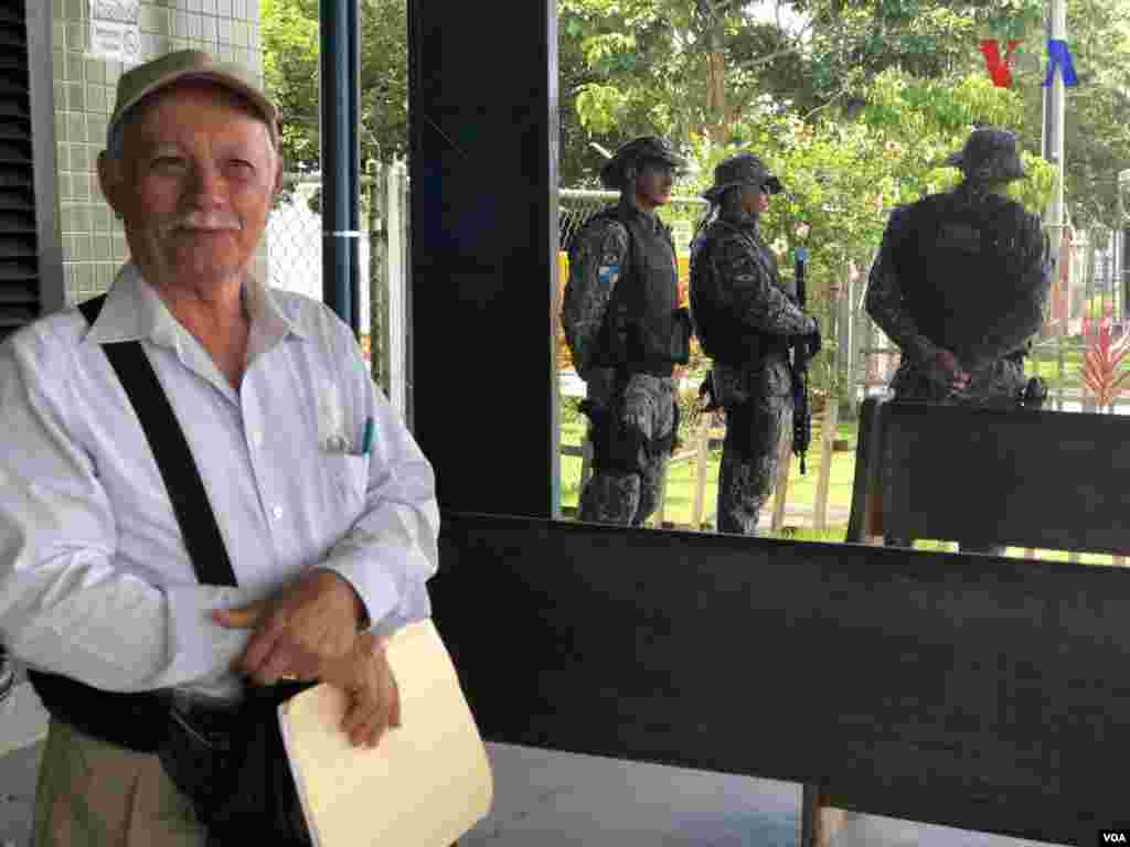 Un señor posa para la foto en la ciudad fronteriza de Pacaraima, Brasil, mientras militares custodian. Foto: Celia Mendoza - VOA.