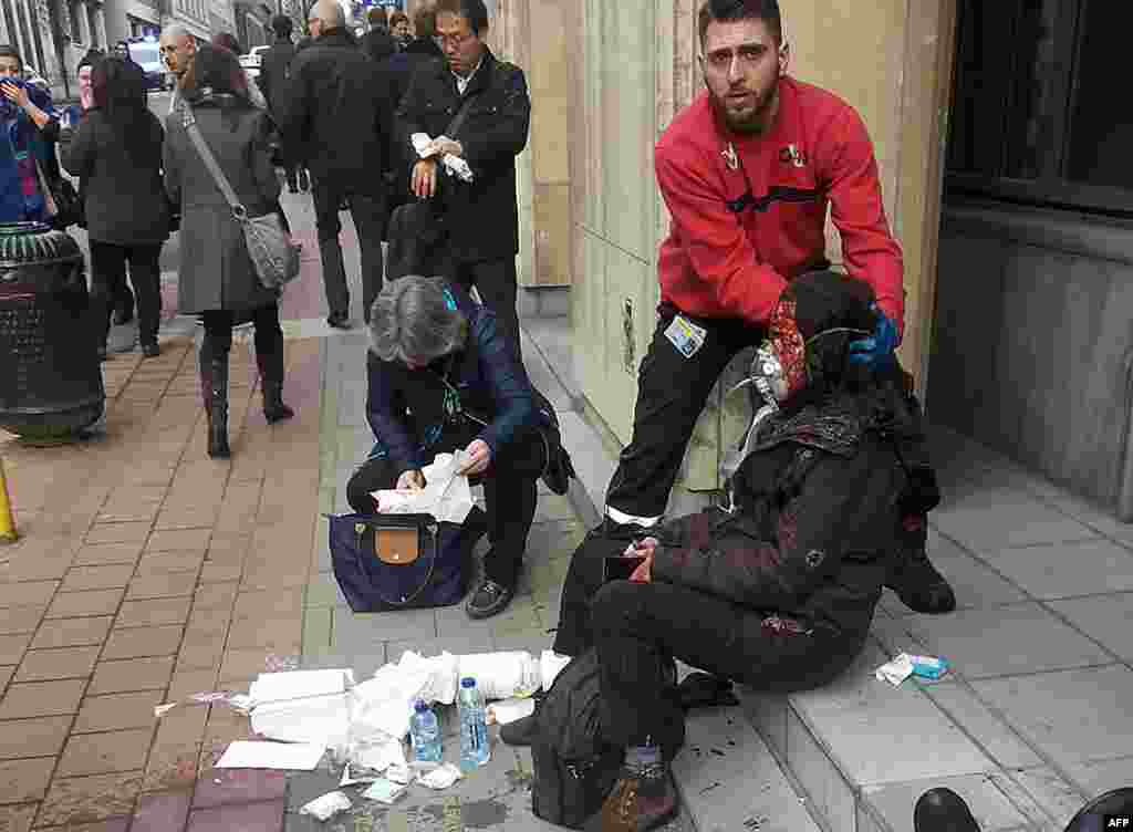 A private security guard helps a wounded women outside the Maalbeek metro station in Brussels on March 22, 2016 after a blast at this station located near the EU institutions.