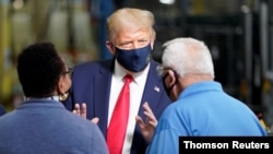 El presidente Donald Trump conversa con dos trabajadores en una planta de producción de la compañía Whirlpool en Clyde, Ohio, el jueves 6 de agosto de 2020.