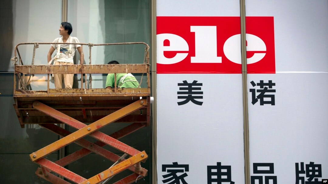Para kerja memasang spanduk untuk pembukaan sebuah toko elektronik di Beijing (15/7). (AP/Mark Schiefelbein)
