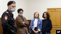 FILE - Editors of the student magazine Doxa wait for a court session as a police officer, left, stands next to them, in Moscow, Russia, April 14, 2021.