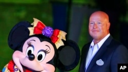 FILE - Chairman of Walt Disney Parks and Resorts Bob Chapek poses with Minnie Mouse during a ceremony at the Hong Kong Disneyland, Sept. 11, 2015.