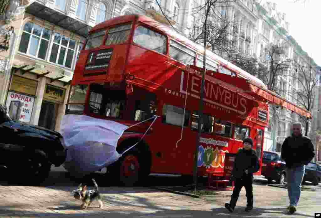 Un hombre y un niño pasan junto a un autobús de dos pisos que se usa como cafetería, simbólicamente con una máscara facial, en Kiev, Ucrania.