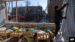 FILE - A man removes a destroyed curtain inside a school damaged among other residential buildings in Kyiv, Ukraine, Friday, March 18, 2022. The Ukrainian government says Russia has shelled more than 1,000 schools, completely destroying 95. (AP Photo/Rodrigo Abd, File)