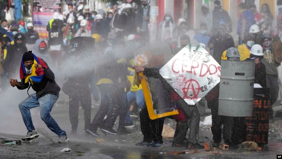 Los manifestantes se protegen de un cañón de agua de la policía durante las protestas contra el gobierno en Bogotá, Colombia, el lunes 28 de junio de 2021.