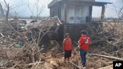 In this photo provided by the Philippine Red Cross, a volunteer talks to a resident beside damaged trees and debris swept by floods caused by Typhoon Usagi in Gonzaga, Cagayan province, northern Philippines on Nov. 15, 2024. 