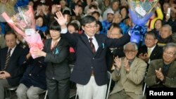 FILE - Mayor Susumu Inamine, center, flanked by his wife, Ritsuko, celebrates his re-election in Nago, Okinawa, Jan. 19, 2014. Inamine, who is opposed to a U.S. Marines base on Okinawa, seeks another term in an election Feb. 4, 2018. 