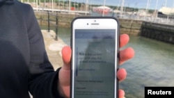 FILE - A National Health Service employee holds up a smartphone displaying a NHS app to trace contacts with people potentially infected with the coronavirus, on the Isle of Wight, Britain, May 5, 2020. 