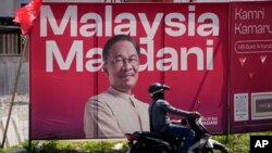 Seorang pengendara motor melintas di depan baliho raksasa dengan foto Perdana Menteri Malaysia Anwar Ibrahim di Kuala Lumpur, Malaysia menjelang pemilu di enam dari 13 negara bagian, Rabu, 9 Agustus 2023. (Foto: Vincent Thian/AP)