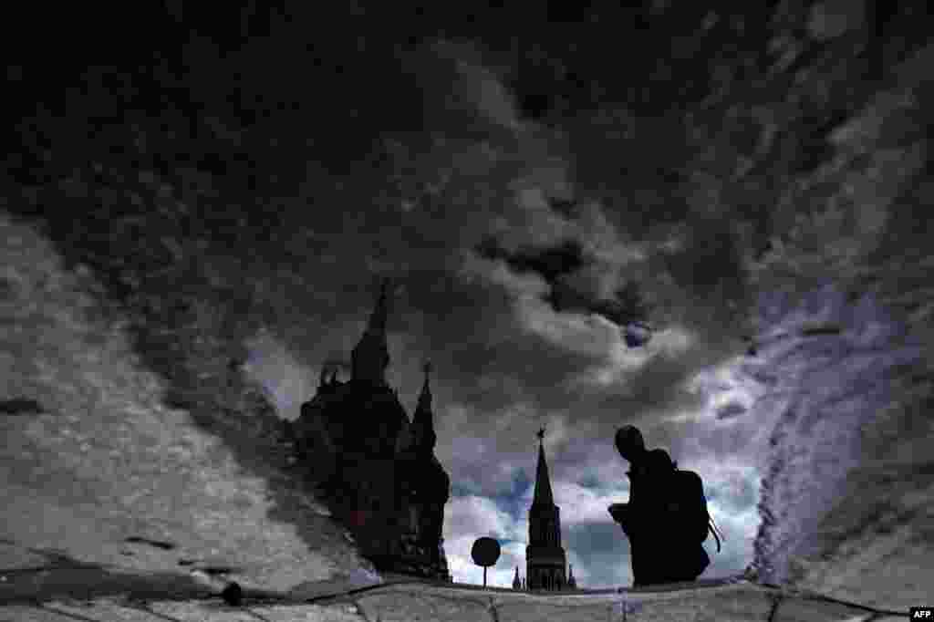 A man is reflected in a puddle as he walks across Moscow&#39;s Red Square, Russia.