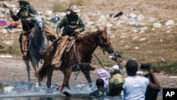 FILE - U.S. Customs and Border Protection mounted officers attempt to contain migrants as they cross the Rio Grande from Ciudad Acuña, Mexico, into Del Rio, Texas, Sept. 19, 2021. 