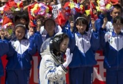 Pelajar China melambaikan bunga dan bendera nasional saat astronot perempuan Wang Yaping meninggalkan pusat peluncuran satelit Jiuquan menuju lokasi peluncuran, dekat Jiuquan, China barat, Selasa, 11 Juni 2013. (Foto: AP/Andy Wong)