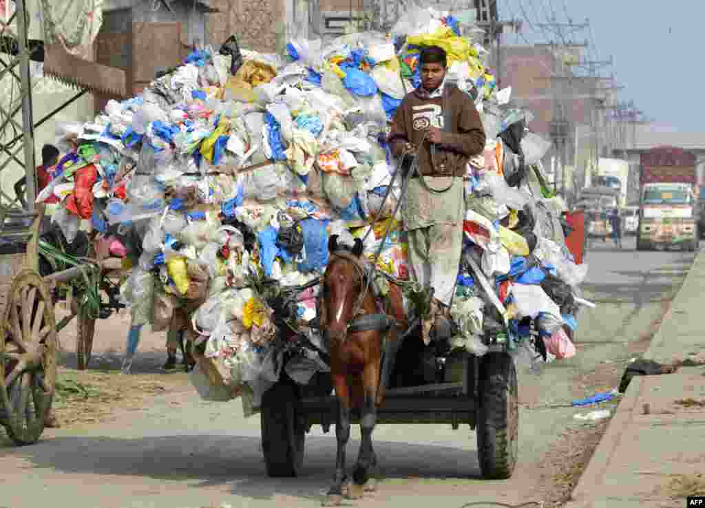 Seorang anak laki-laki membawa kantong-kantong plastik bekas di atas kereta kudanya di kota Lahore, Pakistan.