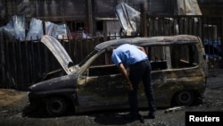 An Israeli man looks at a burnt car parked beside a paint factory in the southern town of Sderot, Israel, June 29, 2014. 