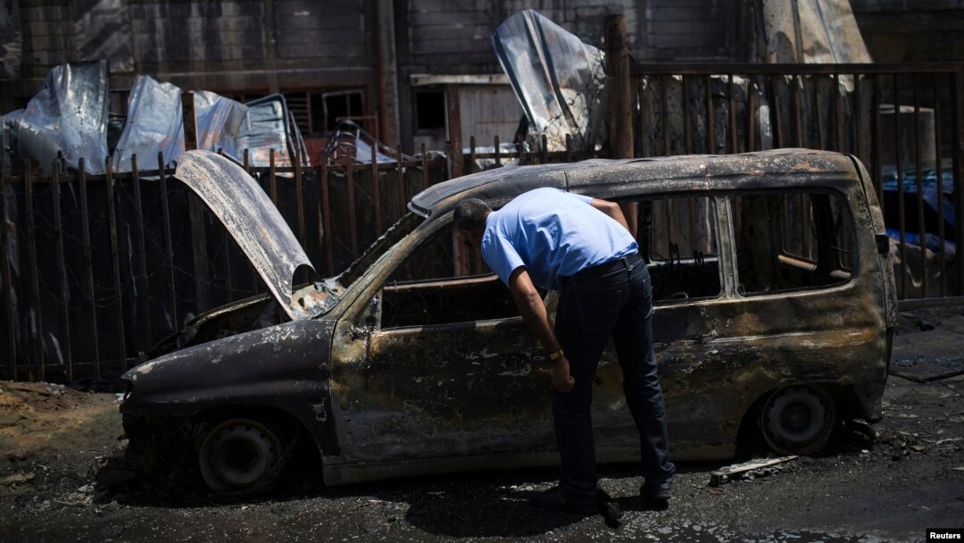 An Israeli man looks at a burnt car parked beside a paint factory in the southern town of Sderot, Israel, June 29, 2014. 