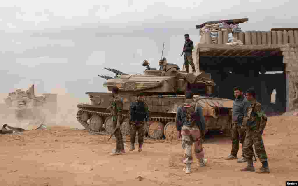 Syrian army soldiers loyal to Syria's President Bashar al-Assad hold their weapons as they stand near a tank in al-Maamel area in Aleppo's countryside, March 25, 2014. 