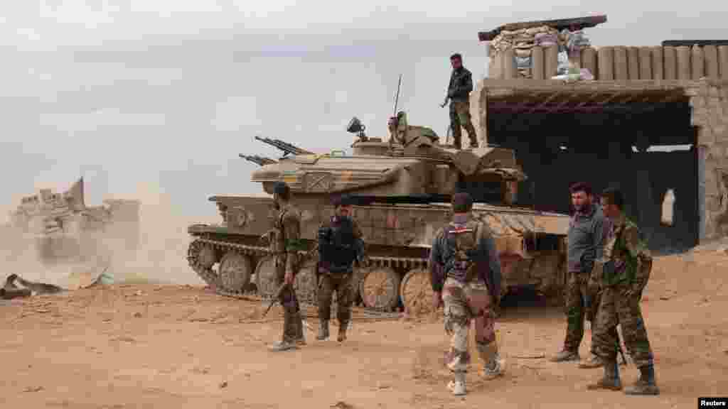 Syrian army soldiers loyal to Syria's President Bashar al-Assad hold their weapons as they stand near a tank in al-Maamel area in Aleppo's countryside, March 25, 2014. 