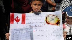 A Palestinian refugee boy holds a placard showing his school report card as hundreds of refugees request asylum at a rally outside the the Canadian Embassy, in Beirut, Lebanon, Sept. 5, 2019.