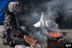 FILE - A displaced Palestinian woman uses a makeshift stove to cook a meal on the street in Rafah in the southern Gaza Strip on February 11, 2024.