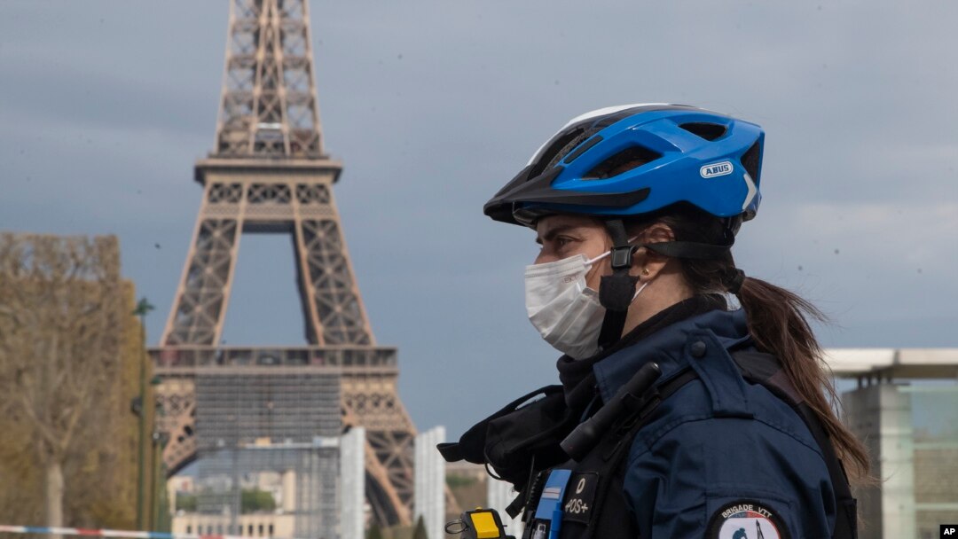 A policewoman wears a mask to protect herself against the spread of the new coronavirus, left, patrols at the garden of the Eiffel Tower in Paris, Monday, April 6, 2020.