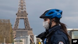 A policewoman wears a mask to protect herself against the spread of the new coronavirus, left, patrols at the garden of the Eiffel Tower in Paris, Monday, April 6, 2020.