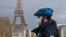A policewoman wears a mask to protect herself against the spread of the new coronavirus, left, patrols at the garden of the Eiffel Tower in Paris, Monday, April 6, 2020.
