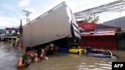 People wade through a flooded road brought about by Tropical Storm Trami in Naga, Camarines Sur, on Oct. 25, 2024. Philippine rescue workers battled floodwaters to reach residents still trapped on the roofs of their homes as Trami moved out to sea. Eleven people died in Naga.