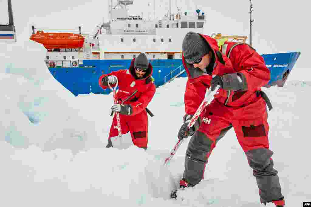 This image taken by expedition doctor Andrew Peacock shows scientists from the University of New South Wales in Australia, Ziggy Marzinellia and Graeme Clark, preparing a suitable surface for a helicopter landing next to the MV Akademik Shokalskiy (background), still stuck in the ice off East Antarctica.