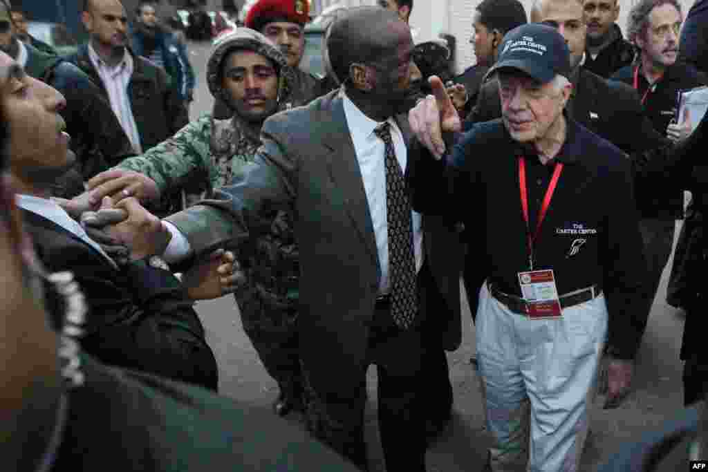 Jimmy Carter (à d) est entouré de gardes de sécurité alors qu'il quitte un bureau de vote au Caire en Egypte le 10 janvier 2012. (Khaled DESOUKI /AFP)