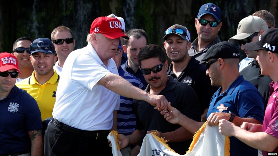 FILE - U.S. President Donald Trump gives out a commemorative "challenge coin" as he plays host to members of the U.S. Coast Guard he invited to play golf at his Trump International Golf Club in West Palm Beach, Fla., Dec. 29, 2017. Administration officials are downplaying any significance of a U.S.-North Korea coin, 250 of which were recently minted.