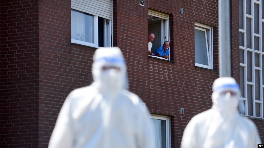 Men look on from a window to personnel of a mobile COVID-19 testing unit of the German Red Cross and the German army (Bundeswehr), prior to testing employees of the abatoir Toennies, at their residential homes in Verl, western Germany, June 23, 2020.