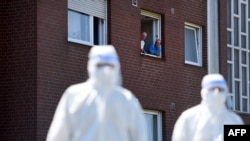 Men look on from a window to personnel of a mobile COVID-19 testing unit of the German Red Cross and the German army (Bundeswehr), prior to testing employees of the abatoir Toennies, at their residential homes in Verl, western Germany, June 23, 2020.