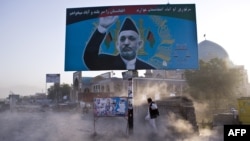 Afghan man shields himself from dust behind a billboard of then-incumbent presidential candidate Hamid Karzai, Kabul, August 13, 2009.