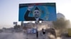 Afghan man shields himself from dust behind a billboard of then-incumbent presidential candidate Hamid Karzai, Kabul, August 13, 2009.