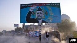 FILE - Afghan man shields himself from dust behind a billboard of Hamid Karzai.