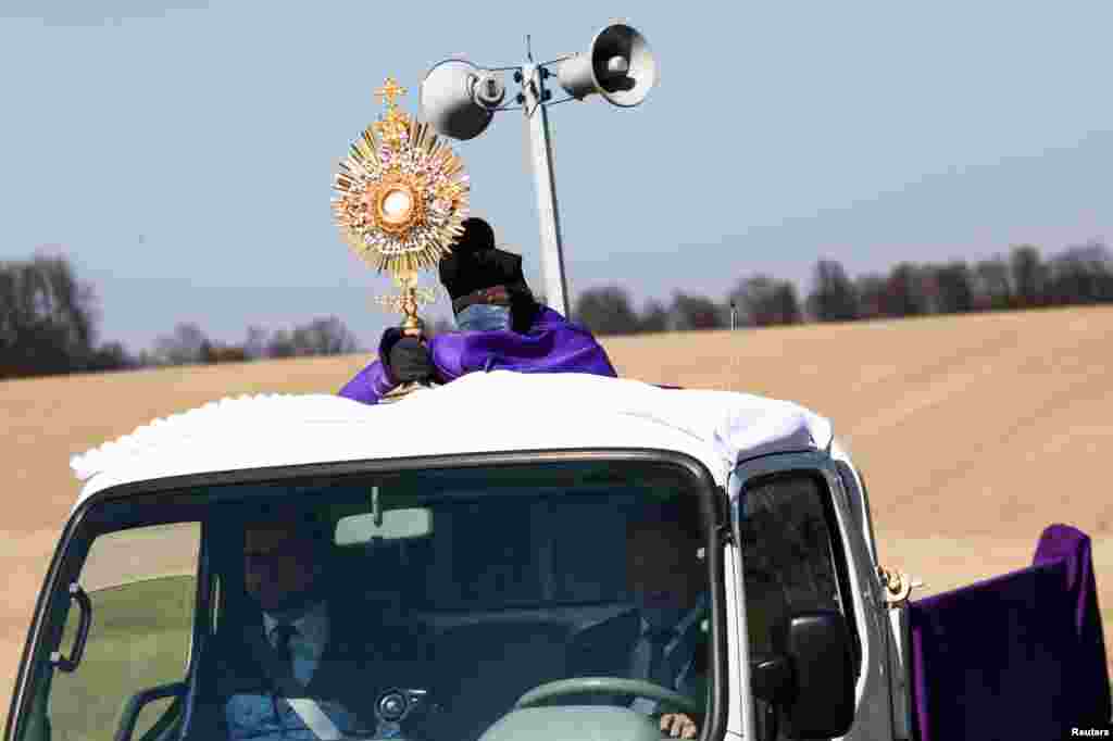 Un sacerdote usa una máscara protectora mientras se para en una camioneta y bendice a los fieles en las aldeas durante el Domingo de Ramos en Nidek, Polonia.