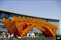 FILE - Workers install wires on a Golden Bridge of Silk Road structure on a platform outside the National Convention Center, the venue for the Belt and Road Forum for International Cooperation, in Beijing, April 18, 2017.