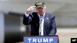 Republican presidential candidate Donald Trump gestures to a his camouflaged "Make America Great" hat as he discuses his support by the National Rifle Association at a campaign rally at the Redding Municipal Airport, June 3, 2016, in Redding, California.