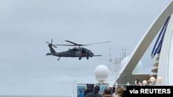 Passengers on board the Grand Princess cruise ship watch while a U.S. military helicopter hovers above the deck, as they approach their original destination of San Francisco, Calif., March 5, 2020.