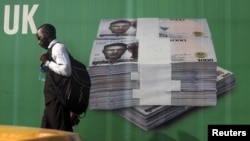A man walks past a promotional banner showing a photograph of a pile of Nigerian naira along a road in Lagos November 24, 2010.