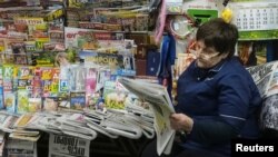 FILE - A woman reads a newspaper and waits for customers as she sells newspapers and magazines at an underground walkway in central Kyiv, Ukraine, Jan. 24, 2019.