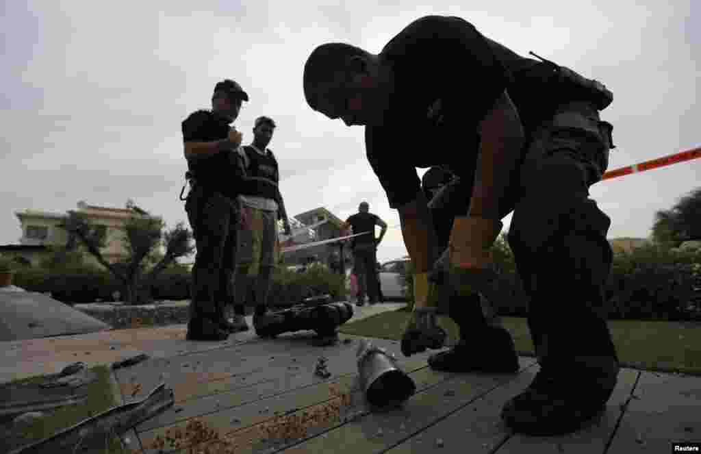 An Israeli police explosives expert reaches for the remains of a rocket, fired by Palestinian militants in Gaza, after it landed in Israel, October 24, 2012.